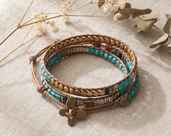 May include: A multi-strand wrap bracelet featuring brown leather cord, turquoise square beads, small round metallic gold beads, and silver-toned accents. The bracelet is secured with a four-petaled flower-shaped metallic button closure.