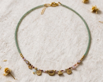 May include: A delicate necklace featuring a strand of small, light green beads accented with gold-toned metal charms. The charms include a small eye, two star-like shapes, a crescent moon, and a triangle, interspersed with tiny pink and white beads.