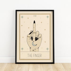Puede incluir: Una impresi&oacute;n enmarcada en negro con un fondo beige y una ilustraci&oacute;n estilizada de una mano haciendo el dedo medio. La mano est&aacute; adornada con anillos y esmalte de u&ntilde;as negro. El texto "XVI THE FINGER" est&aacute; impreso debajo de la mano.