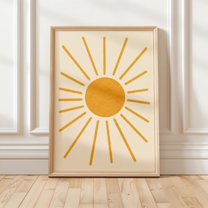 May include: A framed print featuring a minimalist design of a yellow sun with rays radiating outwards on a cream background.