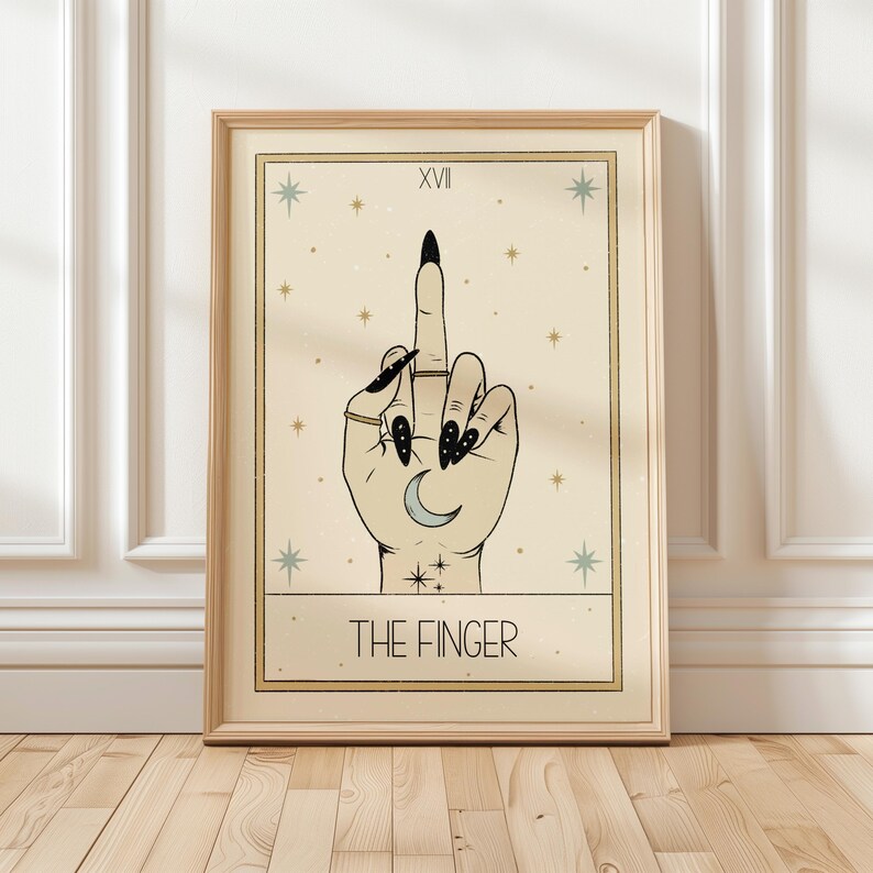 Puede incluir: Una carta del tarot con fondo beige y estrellas doradas. La carta se titula "The Finger" y presenta una mano con esmalte de u&ntilde;as negro haciendo el dedo medio. La mano tiene una luna creciente en la palma.