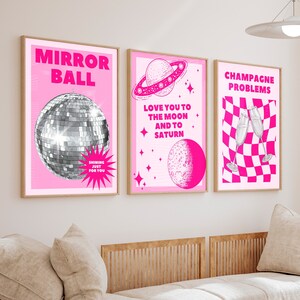 Könnte beinhalten: Drei rosa und weiße gerahmte Drucke mit fettem rosa Text. Der erste Druck sagt "Mirror Ball" und zeigt eine silberne Discokugel. Der zweite Druck sagt "Love you to the moon and to Saturn" und zeigt einen Planeten und einen Mond. Der dritte Druck sagt "Champagne Problems" und zeigt zwei Champagnergläser.