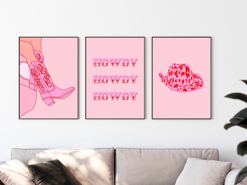 Op de afbeelding: Drie roze en rode ingelijste prints met een roze achtergrond. De linker print toont een paar roze cowboylaarzen met rode stiksels. De middelste print heeft het woord "HOWDY" drie keer herhaald in het rood. De rechter print toont een roze cowboyhoed met een rode luipaardprint.
