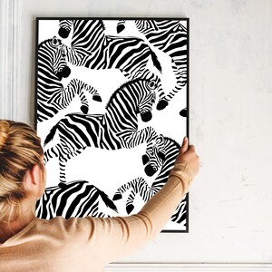 May include: Black and white print of zebras in a repeating pattern. The print is framed and hanging on a white wall.