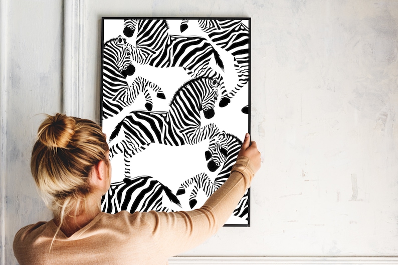 May include: Black and white print of zebras in a repeating pattern. The print is framed and hanging on a white wall.