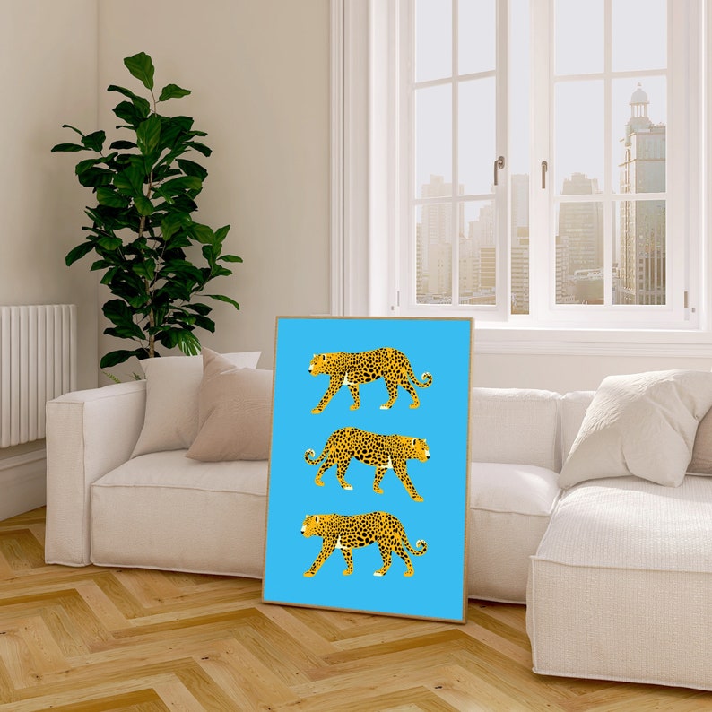 May include: A framed print with a blue background featuring three yellow and black leopards walking in a row. The leopards are facing the right side of the image.