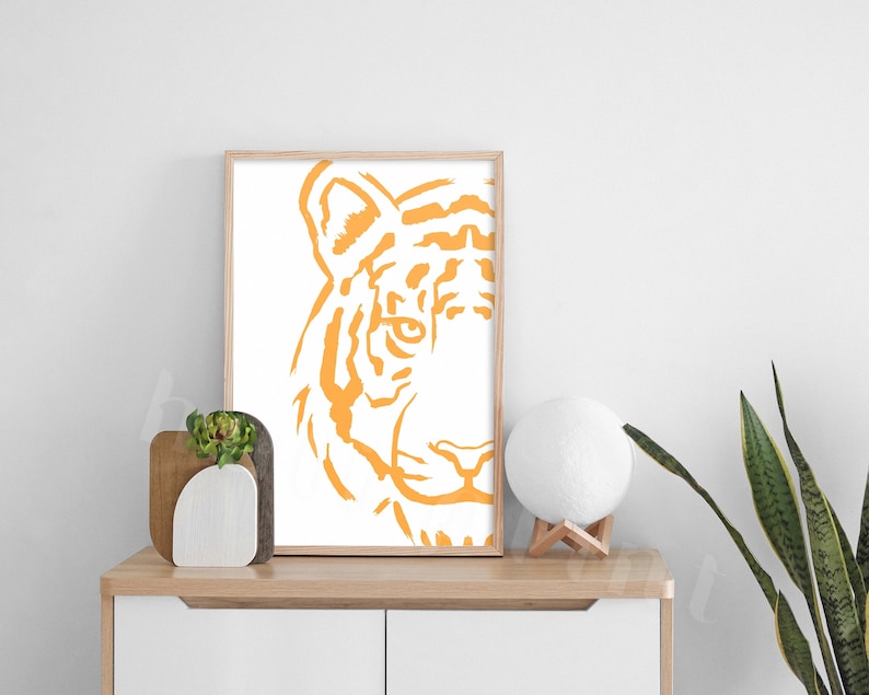 Puede incluir: Una impresi&oacute;n enmarcada de la cara de un tigre en un estilo minimalista. El tigre est&aacute; delineado en naranja sobre un fondo blanco.