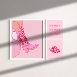 Op de afbeelding: Drie roze en rode ingelijste prints met een roze achtergrond. De linker print toont een roze cowboylaars met rode borduursels. De middelste print heeft het woord "Howdy" drie keer herhaald in het rood. De rechter print toont een roze cowboyhoed met rode vlekken.