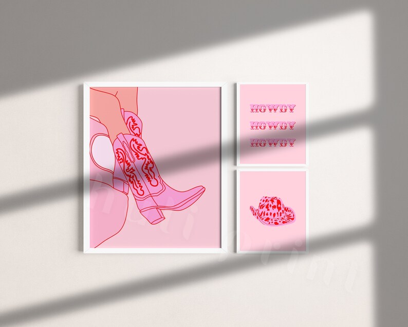 Op de afbeelding: Drie roze en rode ingelijste prints met een roze achtergrond. De linker print toont een roze cowboylaars met rode borduursels. De middelste print heeft het woord "Howdy" drie keer herhaald in het rood. De rechter print toont een roze cowboyhoed met rode vlekken.