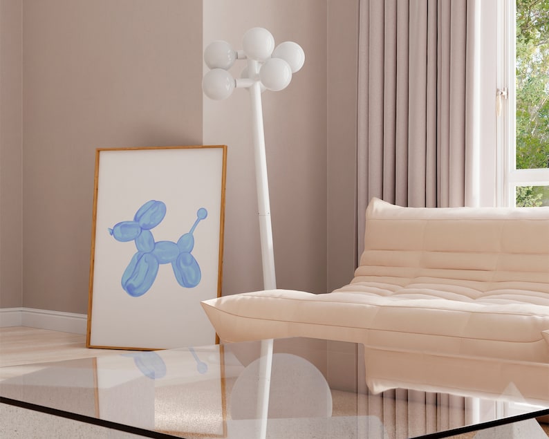 May include: A light blue balloon animal shaped like a dog in a framed print on a white wall with a white floor lamp with white globe lights and a light beige sofa in the background.