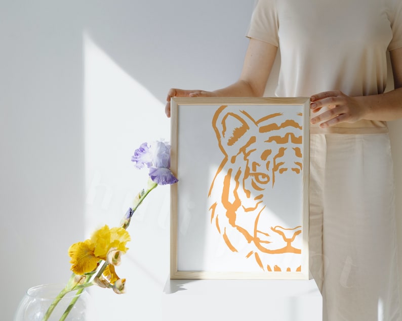 Puede incluir: Una impresi&oacute;n enmarcada de la cara de un tigre en naranja sobre un fondo blanco. La cara del tigre est&aacute; estilizada y tiene un dise&ntilde;o simple.