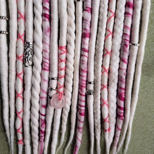 May include: White and pink wool dreadlocks with silver beads and a pink stone charm.