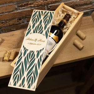Könnte beinhalten: Eine Holzkiste für Wein mit einem grünen Laser-Schnittmuster und dem Text "Adam & Anna 12. September 2027". Die Kiste ist geöffnet und eine Flasche Wein befindet sich darin.