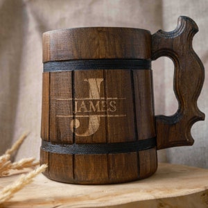 May include: A wooden beer stein with a dark brown finish. The stein has a handle and is engraved with the name "JAMES" and the letter "J".