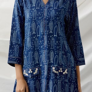 May include: A blue cotton tunic dress with a white fish print and pearl-like button embellishments on the pockets.