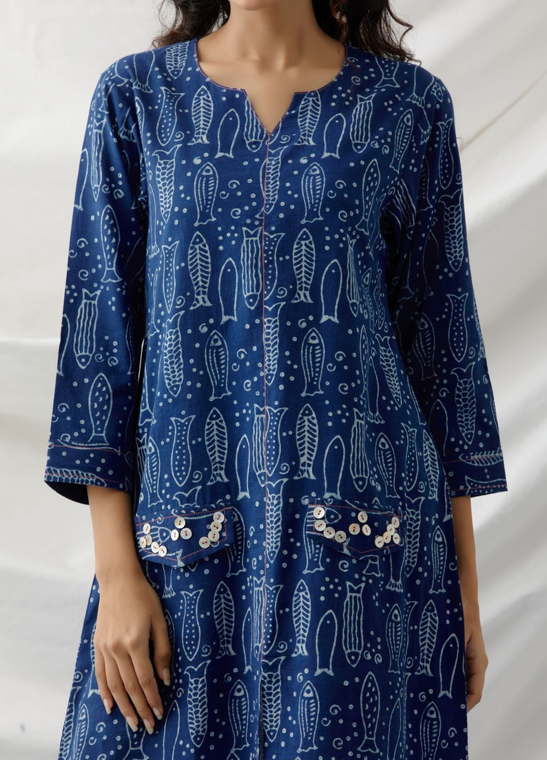 May include: A blue cotton tunic dress with a white fish print and pearl-like button embellishments on the pockets.