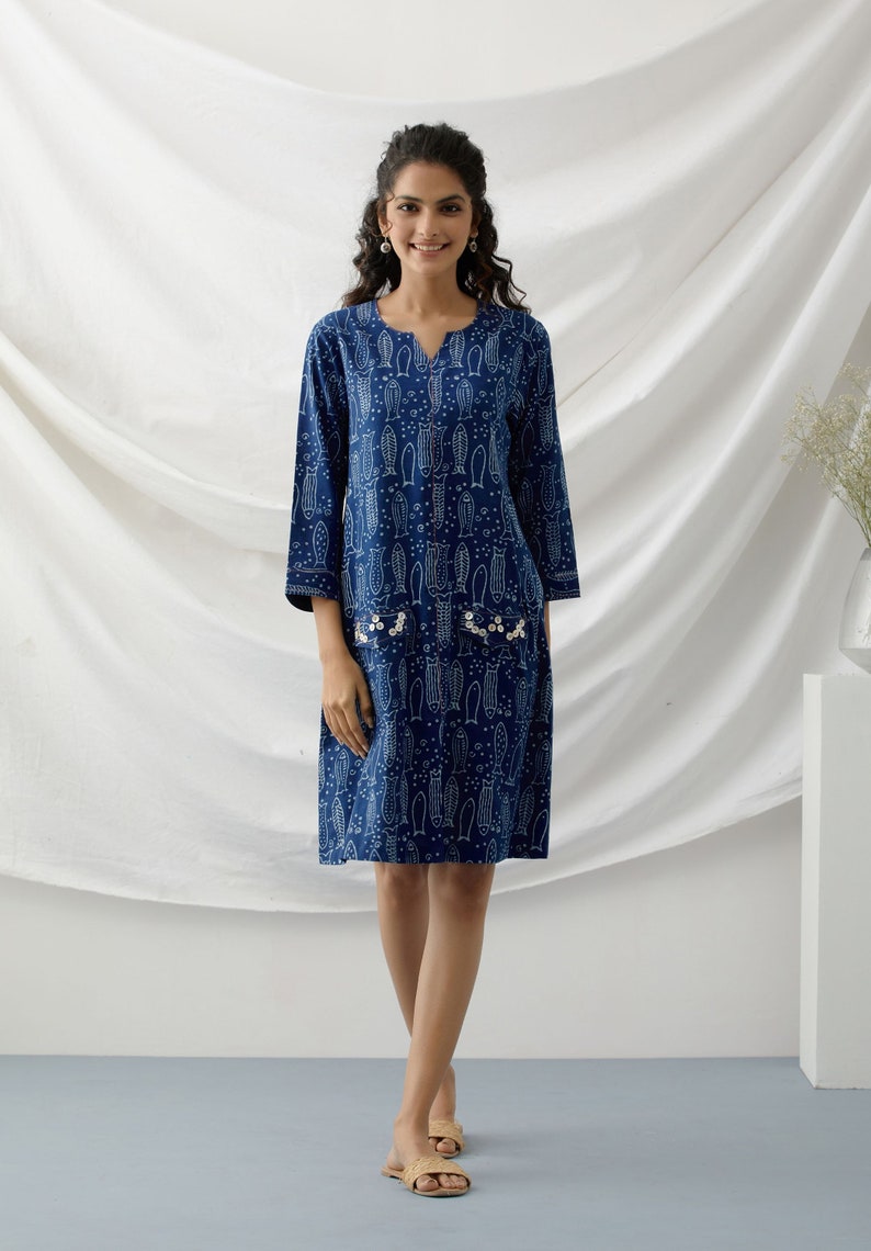 May include: A blue and white printed cotton dress with a V-neckline and three-quarter sleeves. The dress has a pocket on each side with pearl embellishments.
