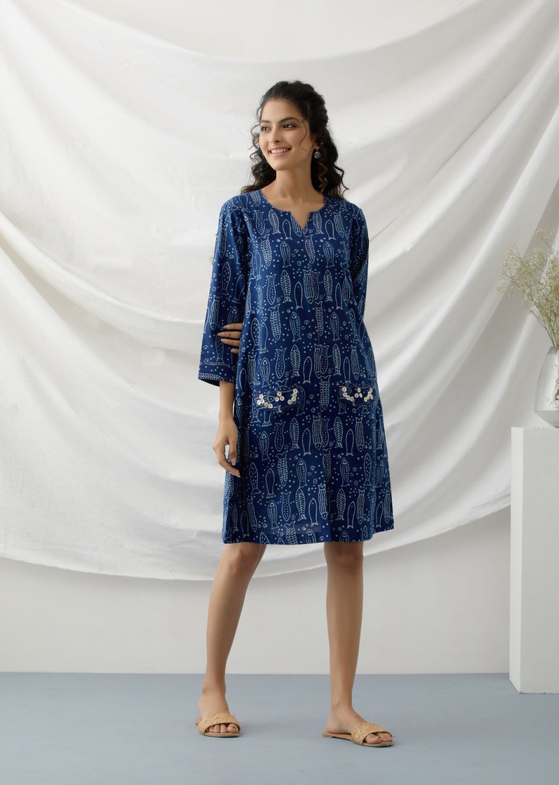 May include: A blue cotton dress with a white fish print and pearl embellishments. The dress has a v-neck and three-quarter sleeves.