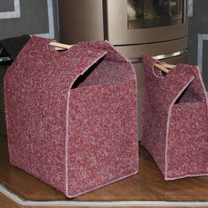 Könnte beinhalten: Zwei rote Filz-Aufbewahrungskörbe mit Holzgriffen. Die Körbe stehen auf einem Holzboden vor einem Kamin.