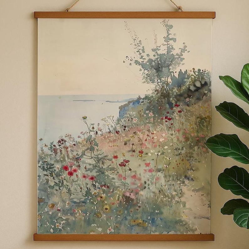 May include: Watercolor landscape print featuring a coastal scene with wildflowers and a tree. The artwork is displayed on a wooden frame with a hanging rope. The color palette includes shades of blue, green, pink, and beige.