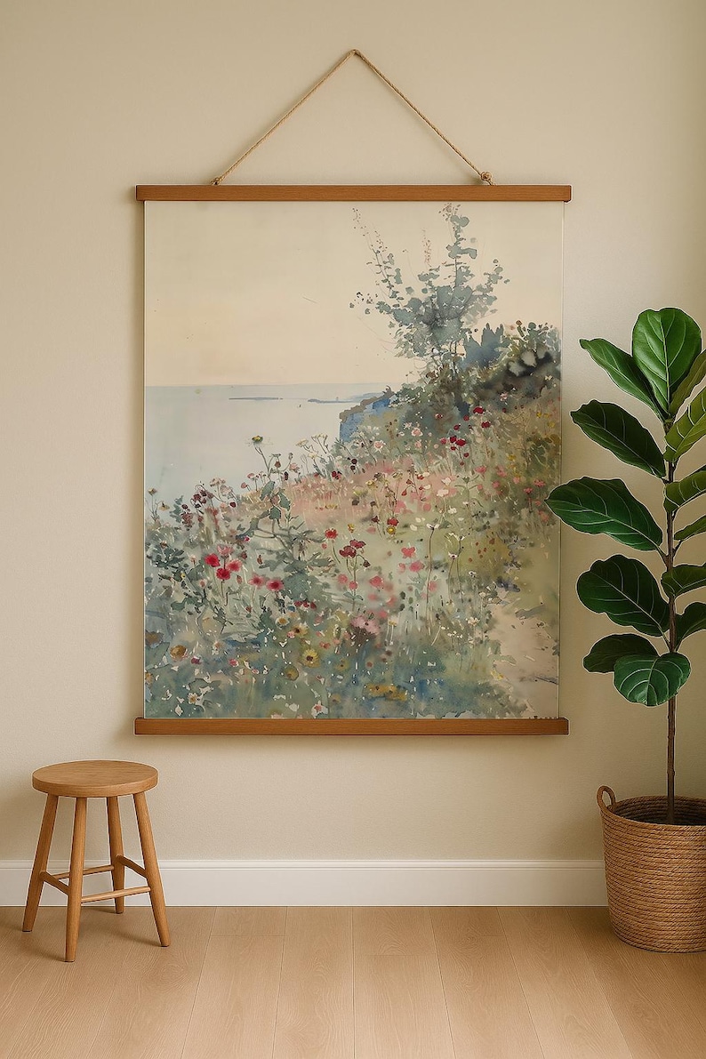 May include: Watercolor landscape art print featuring a coastal scene with colorful wildflowers and a tree. The artwork is displayed on a wooden frame and hung by a rope. A wooden stool and a potted plant are in the foreground.
