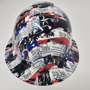 May include: A hard hat featuring a patriotic graphic pattern in red, white, and blue. The design includes repeated text segments of the United States Constitution, specifically the phrase We the People and the 2nd Amendment, overlaid on stars.