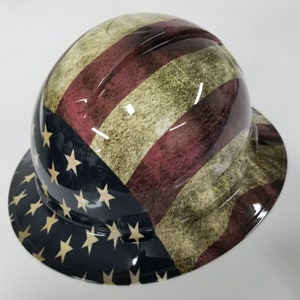 May include: A hard hat with a distressed American flag design. The hat is black with white stars and red and white stripes. The stripes are faded and have a distressed look.