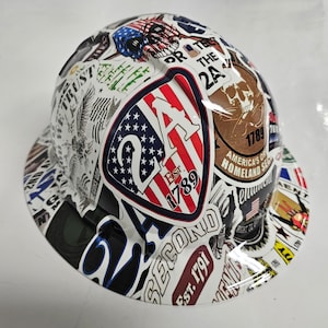 May include: White hard hat with a variety of colorful stickers, including a large American flag sticker with the text "2A Est. 1789" and other stickers with text like "America's Original Homeland Security" and "Est. 1791 Second".