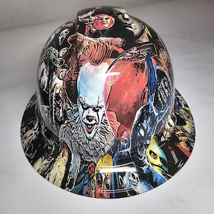 May include: A hard hat with a colorful graphic design featuring characters from horror movies. The design includes Pennywise the clown, a creature from the movie Alien, and other horror movie characters.