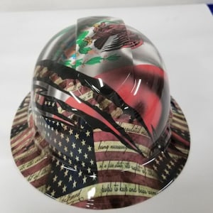 May include: A hard hat with a graphic design featuring the American and Mexican flags, along with the text "being necessary of a free state, the right of the people to keep and bear arms".