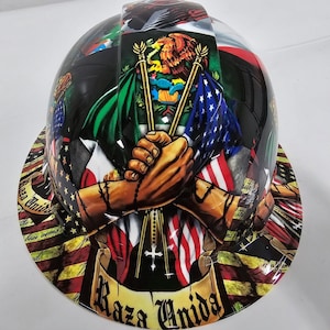 May include: A black hard hat featuring a design with the flags of the United States and Mexico, clasped hands, and the words "Raza Unida". The design includes a cross and rosary beads.