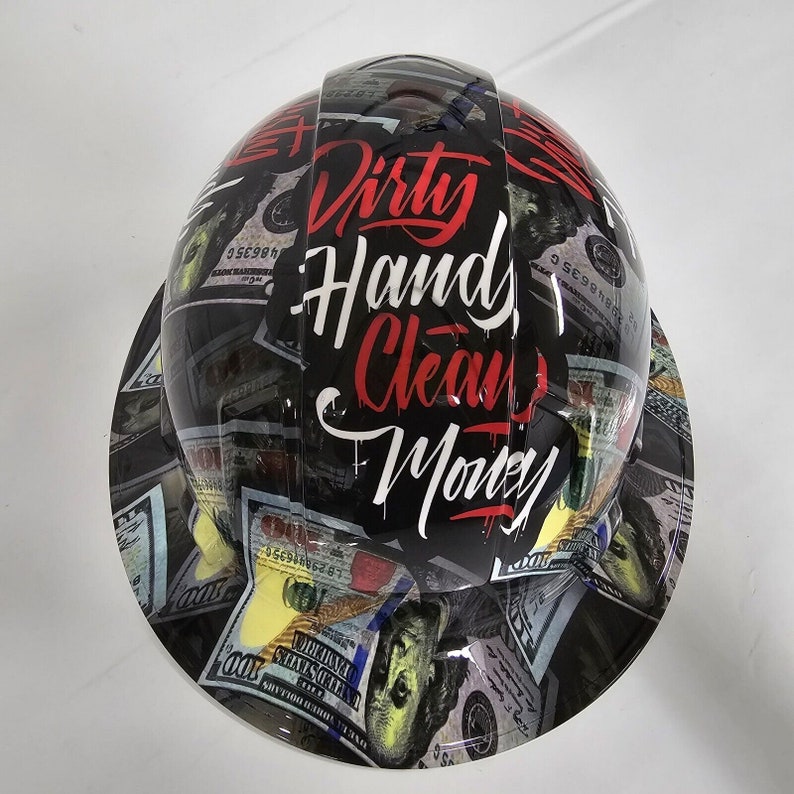 May include: A black hard hat with a design of dollar bills and the words "Dirty Hands, Clean Money" in red and white lettering.