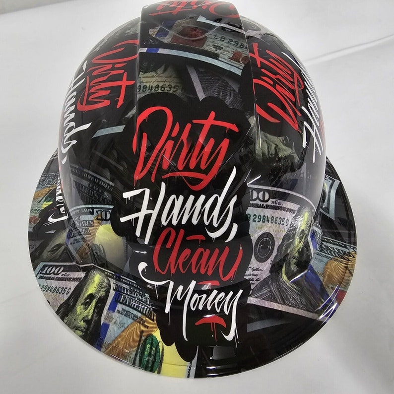 May include: A black hard hat with a white brim, covered in a pattern of US dollar bills. The text "Dirty Hands, Clean Money" is written in red and white on the front of the hat.