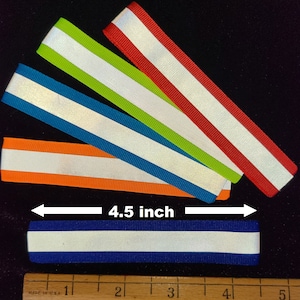 K&ouml;nnte beinhalten: F&uuml;nf reflektierende Bandstreifen in verschiedenen Farben, darunter Orange, Blau, Gr&uuml;n und Rot, mit einem wei&szlig;en reflektierenden Streifen in der Mitte. Die Bandstreifen sind 4,5 Zoll lang.