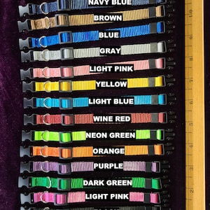 May include: A set of 15 solid colour dog collars in various colours, including red, navy blue, brown, blue, grey, light pink, yellow, light blue, wine red, neon green, orange, purple, dark green, light pink, and black. The collars are arranged vertically with the colour names printed below each collar. The text "SOLID COLOR COLLARS" is printed at the bottom of the image.