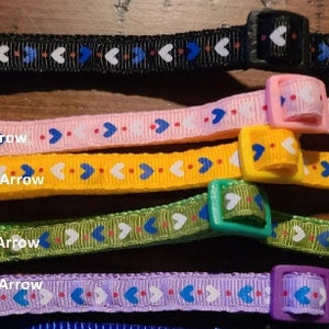 May include: Five colourful adjustable collars with arrow and heart patterns. The collars are black, pink, yellow, green, and purple. Each collar has a plastic buckle.