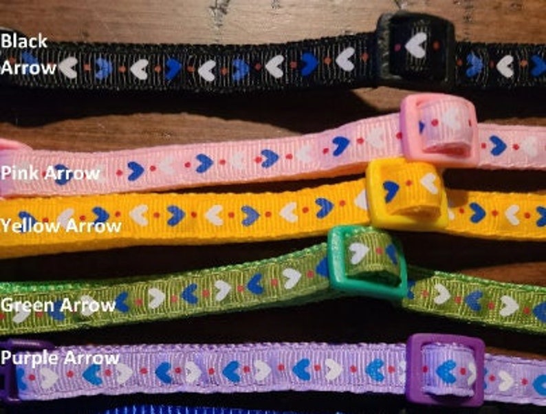 May include: Five colourful adjustable collars with arrow and heart patterns. The collars are black, pink, yellow, green, and purple. Each collar has a plastic buckle.