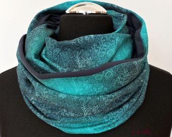 May include: A teal blue infinity scarf with a white floral pattern. The scarf is made of a soft, stretchy fabric and has a dark gray trim.
