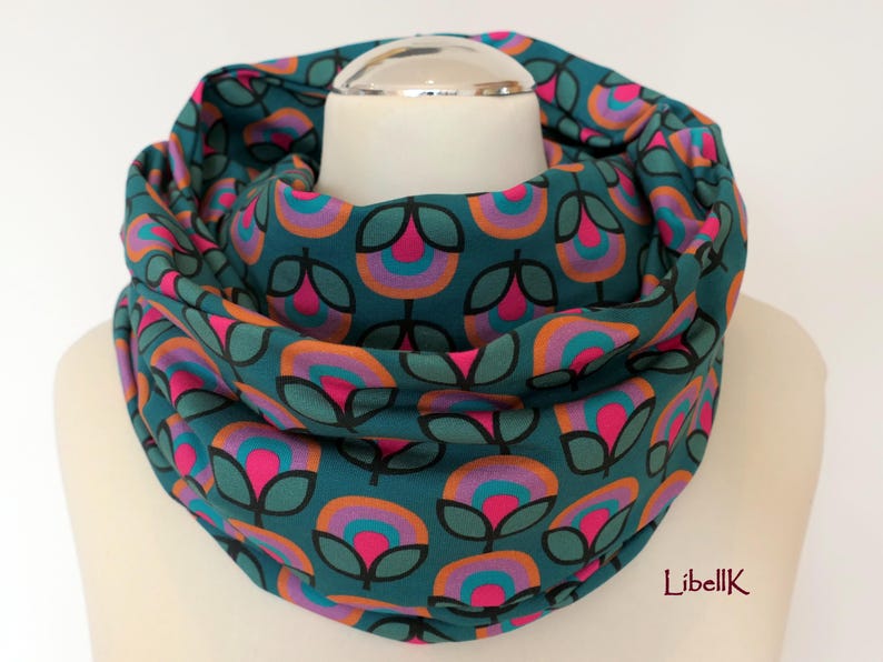 May include: Teal infinity scarf with a repeating pattern of pink, orange, and turquoise flowers. The scarf is made of a soft, comfortable fabric and is perfect for keeping warm in the winter.