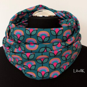 May include: A teal blue infinity scarf with a repeating pattern of pink, orange and purple flowers. The scarf is folded and displayed on a mannequin.