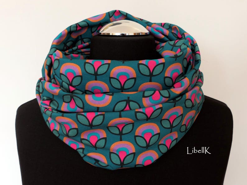 May include: A teal blue infinity scarf with a repeating pattern of pink, orange and purple flowers. The scarf is folded and displayed on a mannequin.
