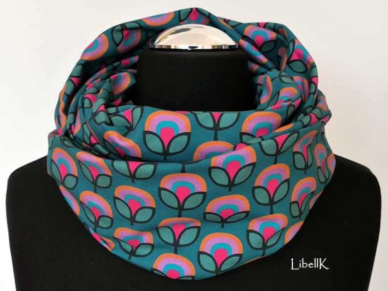 May include: A teal blue infinity scarf with a repeating pattern of pink, orange, and turquoise flowers.