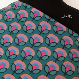 May include: Teal fabric with a repeating pattern of stylised flowers in shades of pink, orange, purple, and teal. The fabric has a black waistband with the text "LibellK" printed on it.