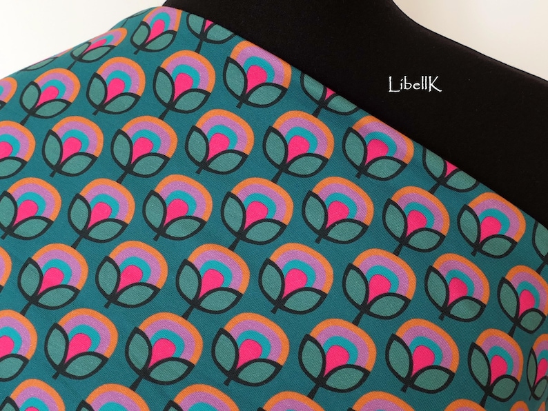 May include: Teal fabric with a repeating pattern of stylised flowers in shades of pink, orange, purple, and teal. The fabric has a black waistband with the text "LibellK" printed on it.