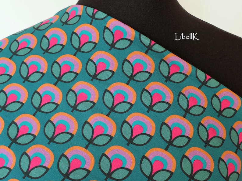 May include: Teal fabric with a repeating pattern of stylised flowers in shades of pink, orange, and purple. The flowers have a retro, 70s aesthetic.