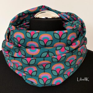 May include: Teal blue infinity scarf with a repeating pattern of pink, orange and purple flowers. The flowers have a retro, 70s style.