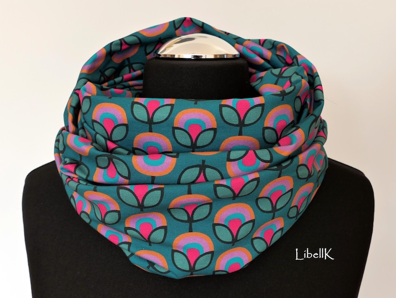 May include: Teal blue infinity scarf with a repeating pattern of pink, orange and purple flowers. The flowers have a retro, 70s style.