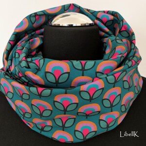 May include: Teal blue infinity scarf with a repeating pattern of pink, orange, and teal flowers. The scarf is folded and displayed on a black mannequin.