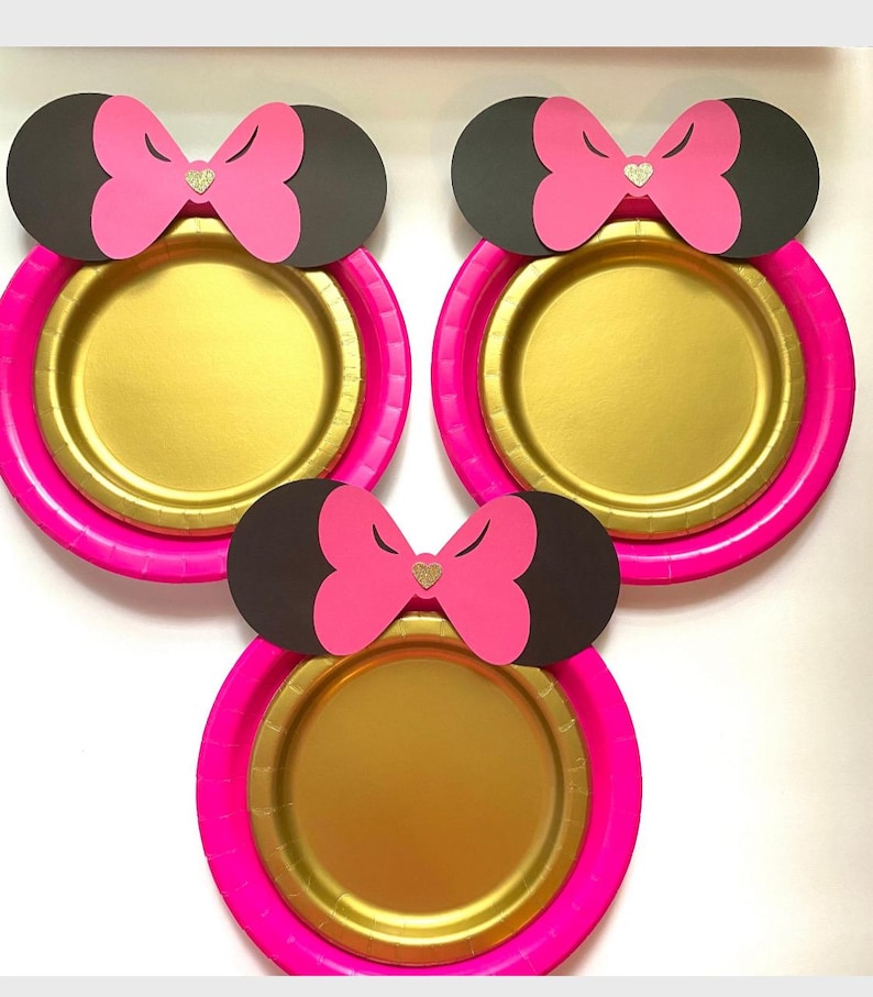 May include: Three gold paper plates with pink rims and black mouse ears with pink bows and gold glitter hearts.