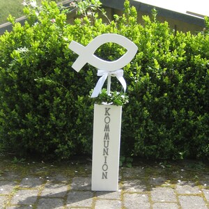 以下が含まれることがあります： 白い木製の看板に「COMMUNION」という文字が印刷されています。白い木製の魚のシンボルが、白いリボンで看板の上部に付けられています。